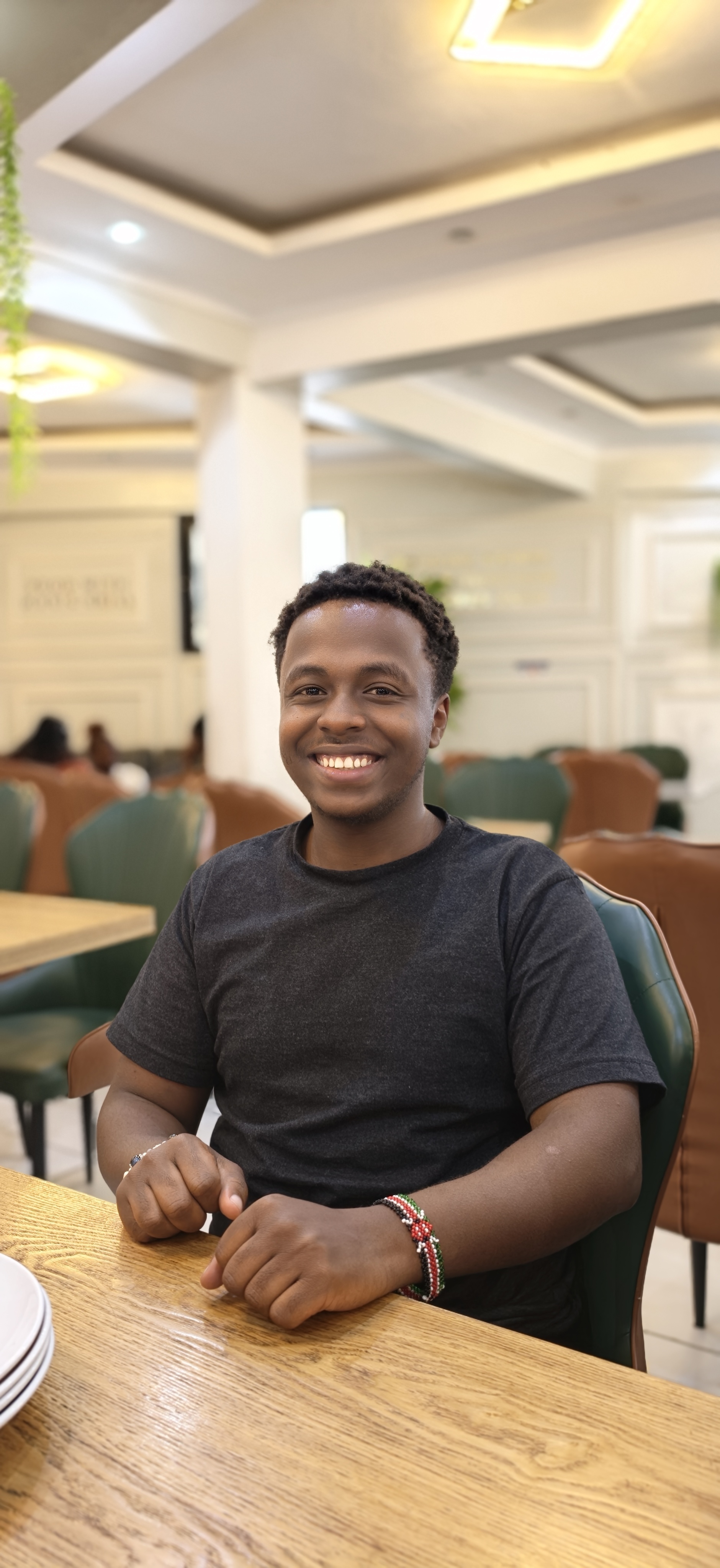 Dickson Ngure smiling, seated at a table, wearing a Kenyan beaded bracelet